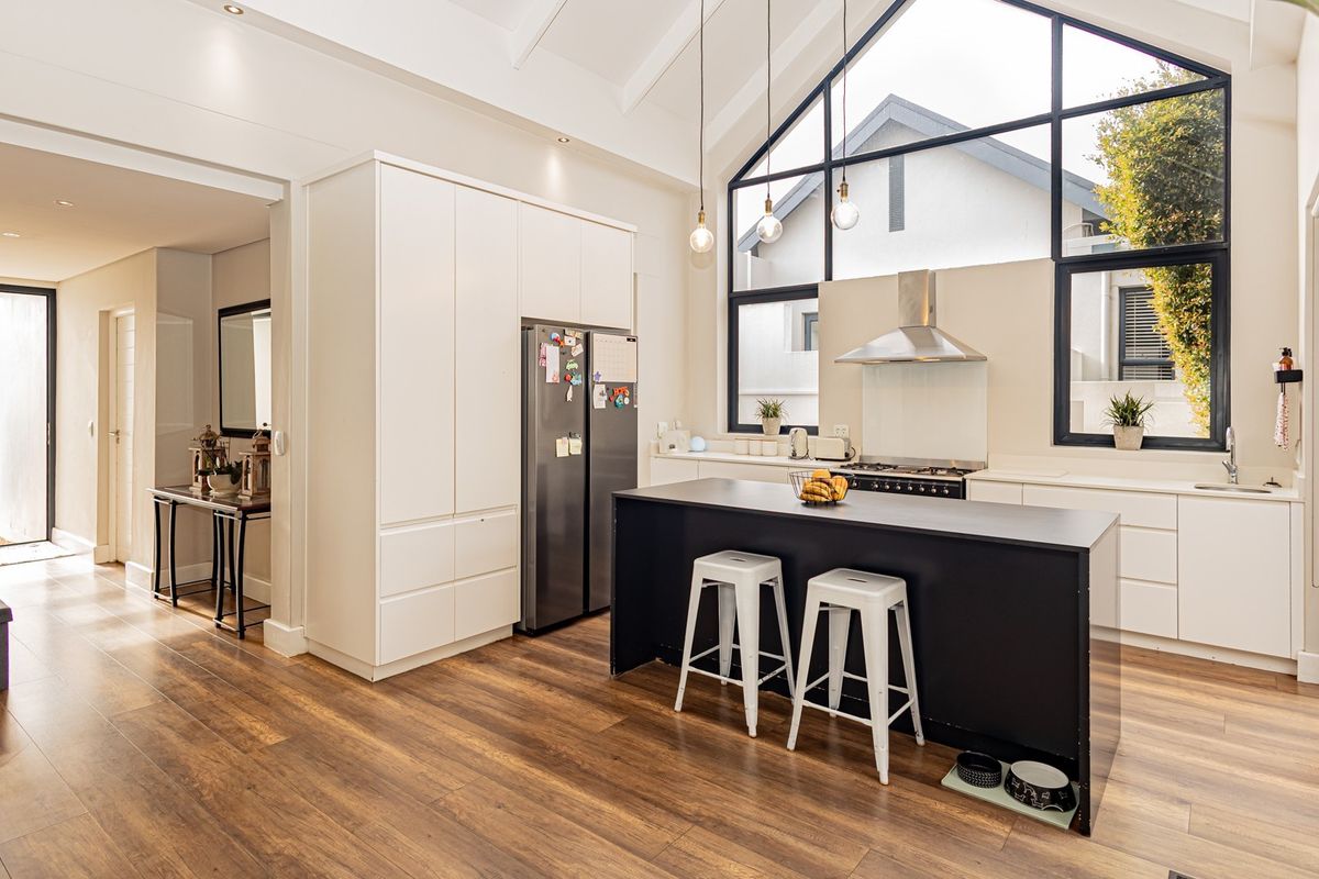 Modern open-plan kitchen featuring a central island, high vaulted ceilings, large feature windows, and sleek cabinetry with integrated appliances.