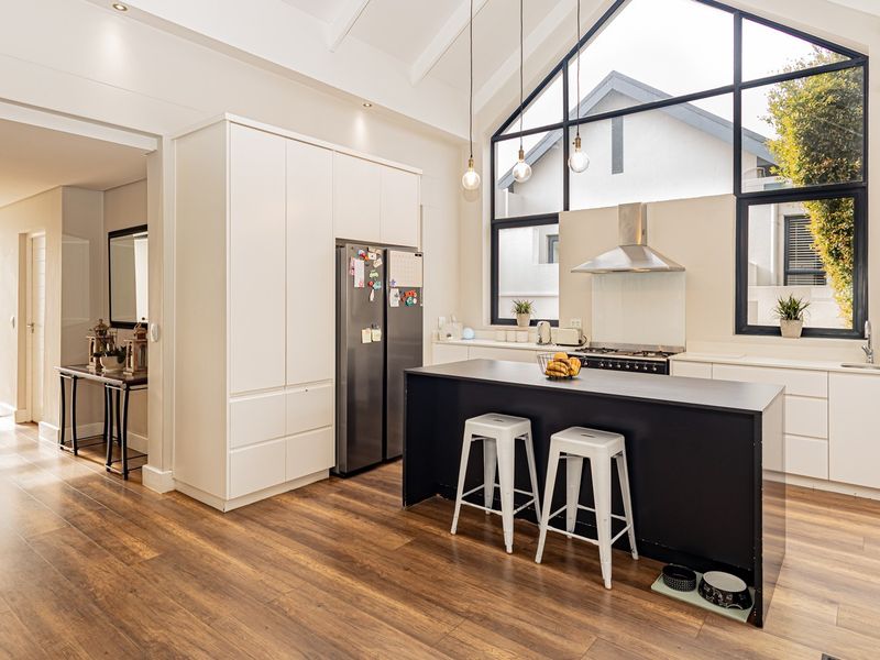 Modern open-plan kitchen featuring a central island, high vaulted ceilings, large feature windows, and sleek cabinetry with integrated appliances.