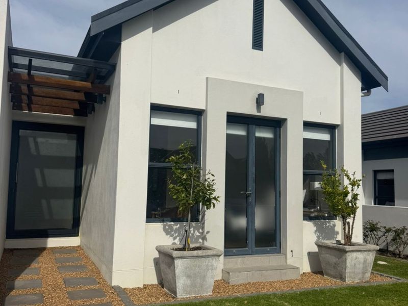 A modern rear exterior view featuring a clean white facade, dark window frames, a timber pergola, and a well-maintained garden with a paved walkway.