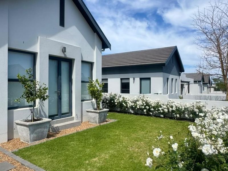 A well-maintained rear exterior view featuring a landscaped garden, paved walkway, and modern house facade with french doors and tiled roofing.