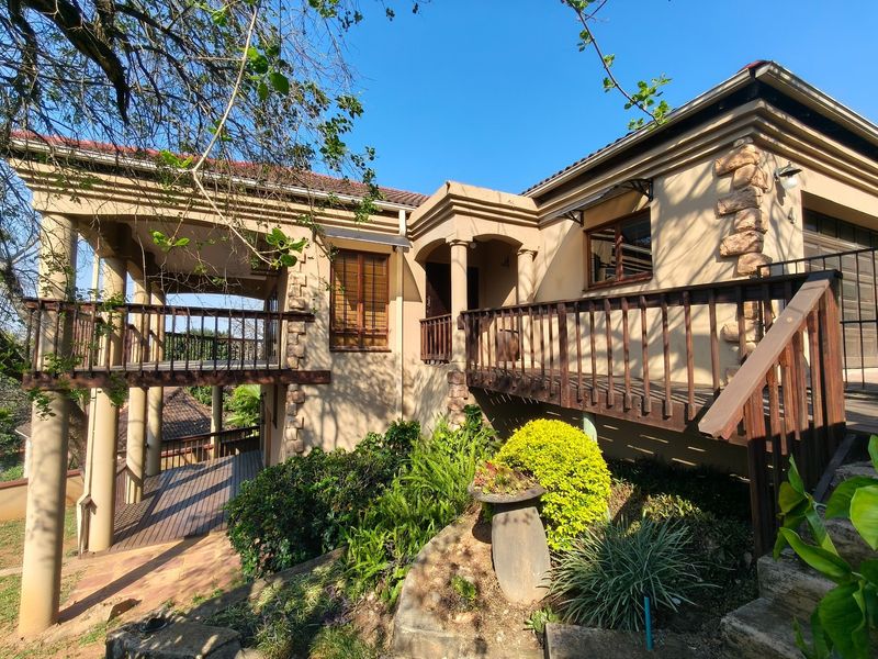 Rear elevation of the house featuring a raised wooden deck, covered patio area, stone accents, and established garden landscaping.