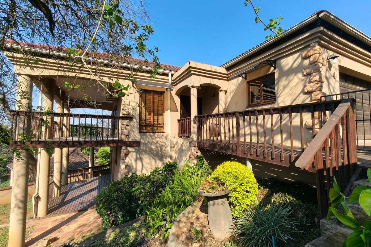 Rear elevation of the house featuring a raised wooden deck, covered patio area, stone accents, and established garden landscaping.