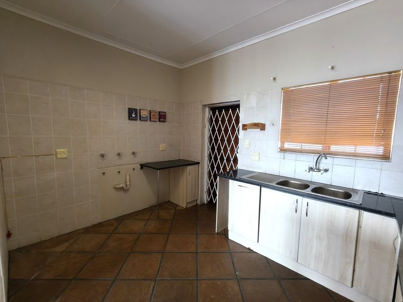 A functional kitchen space featuring tiled flooring, a double bowl sink, built-in base cabinetry, and a security gate leading to the exterior.