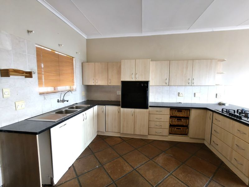 A functional kitchen featuring light wood-finish cabinetry, granite countertops, a built-in oven, gas hob, and double sink with tiled flooring.