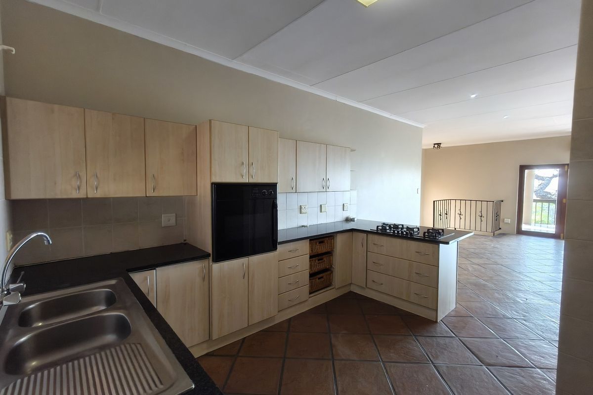 Spacious kitchen featuring light wood cabinetry, built-in oven, gas hob, and dark stone countertops, flowing into an open-plan living area with tiled floors.