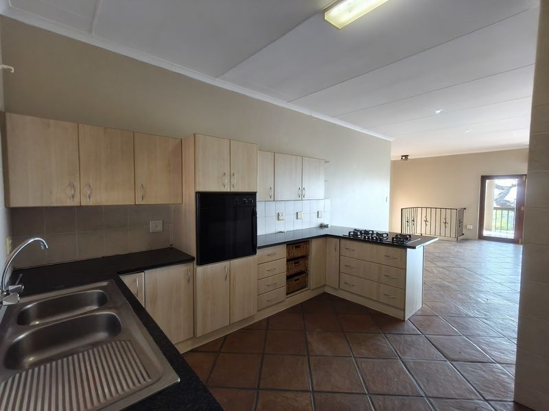 Spacious kitchen featuring light wood cabinetry, built-in oven, gas hob, and dark stone countertops, flowing into an open-plan living area with tiled floors.