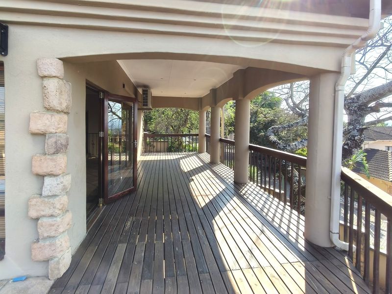 A spacious covered balcony featuring timber decking, stone pillar accents, and a wooden railing, offering an ideal outdoor space for relaxation.