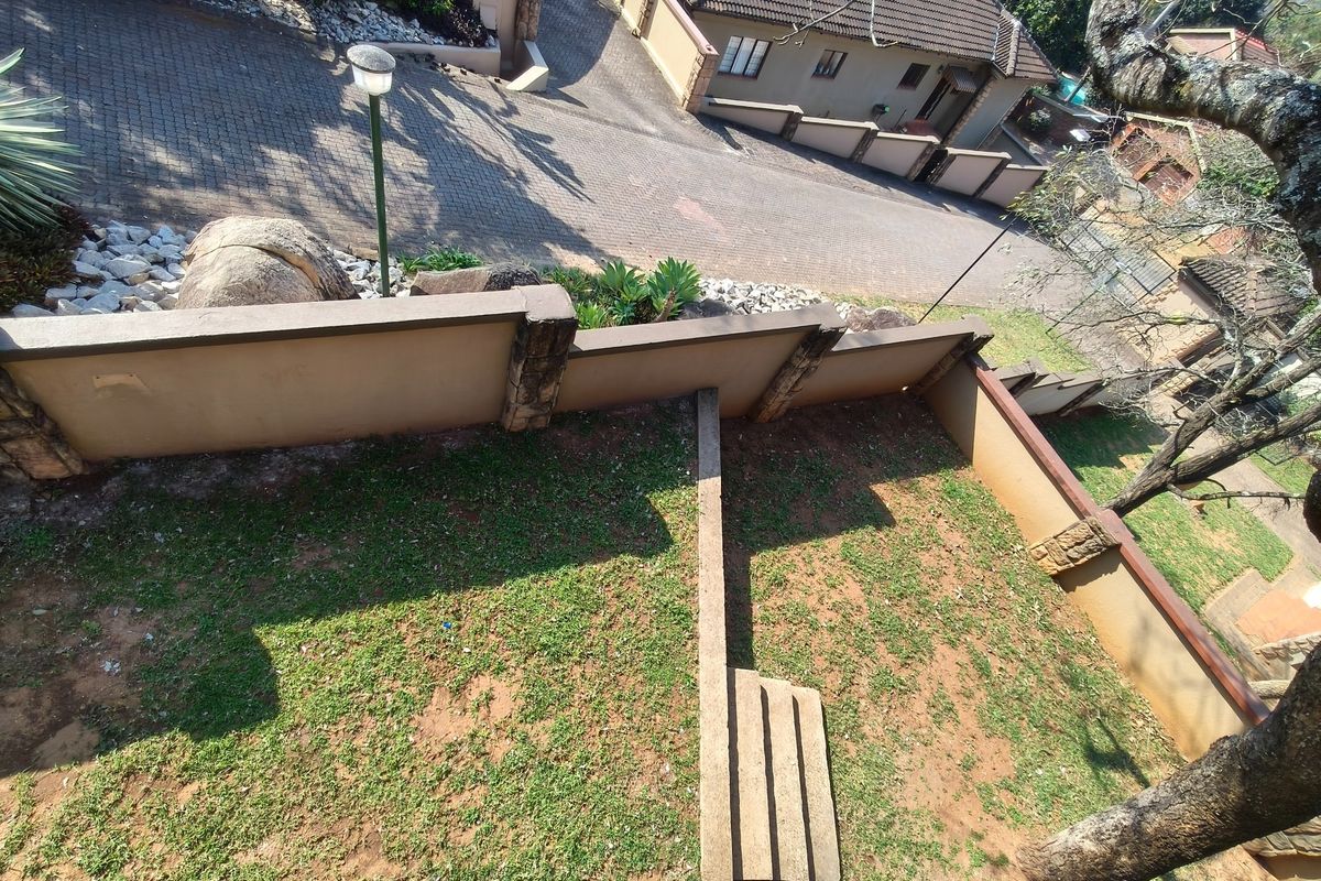 An elevated view of the property grounds featuring a retaining wall, paved driveway, and garden area with concrete steps.