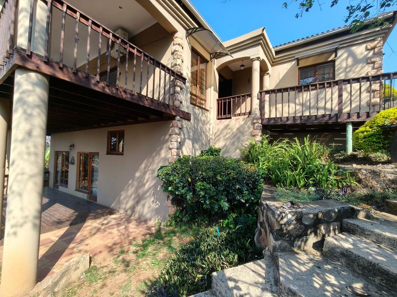 Rear elevation of the house featuring a multi-level wooden balcony, stone cladding accents, and a landscaped garden with stone stairs.