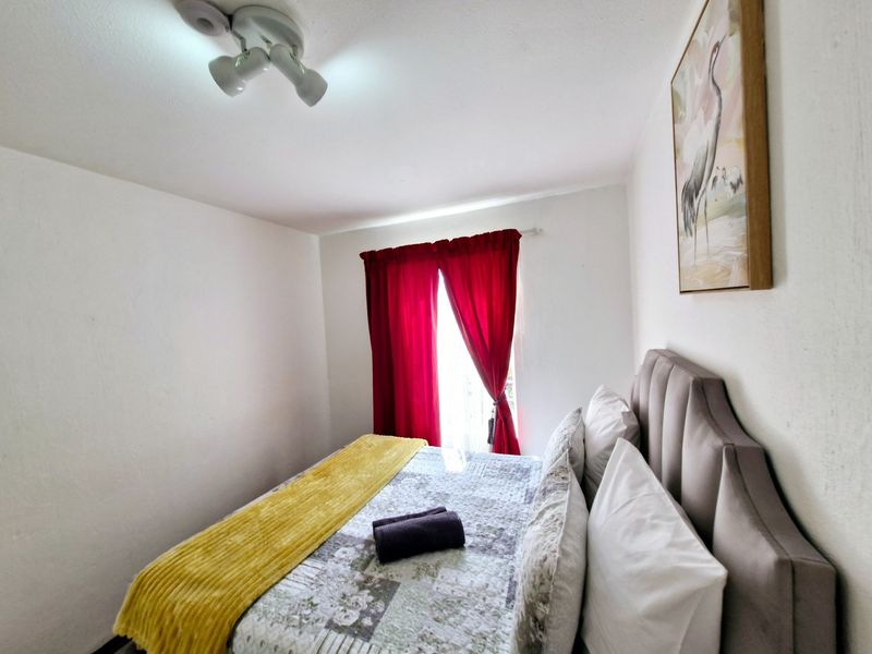 A functional bedroom featuring a ceiling-mounted light fixture and a window with red curtains, providing a simple and comfortable sleeping space.