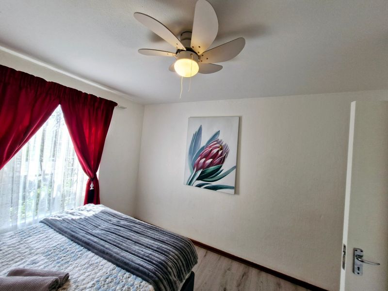 A well-maintained bedroom featuring modern laminate flooring, a central ceiling fan, and neutral wall finishes.