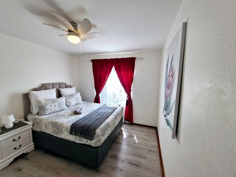 A well-maintained bedroom featuring light-toned laminate flooring, a ceiling fan, and neutral wall finishes.