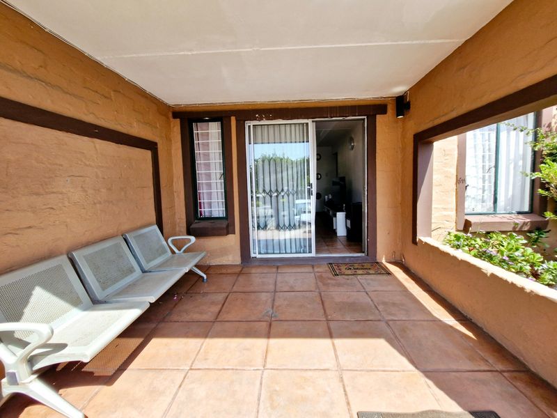 A covered patio area featuring tiled flooring, a built-in planter box, and a sliding glass door with security gate access to the interior.