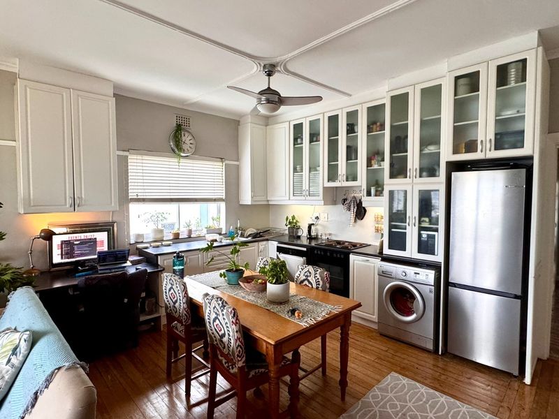 Open-plan kitchen and living area featuring white cabinetry, hardwood flooring, integrated appliances, and a ceiling fan.