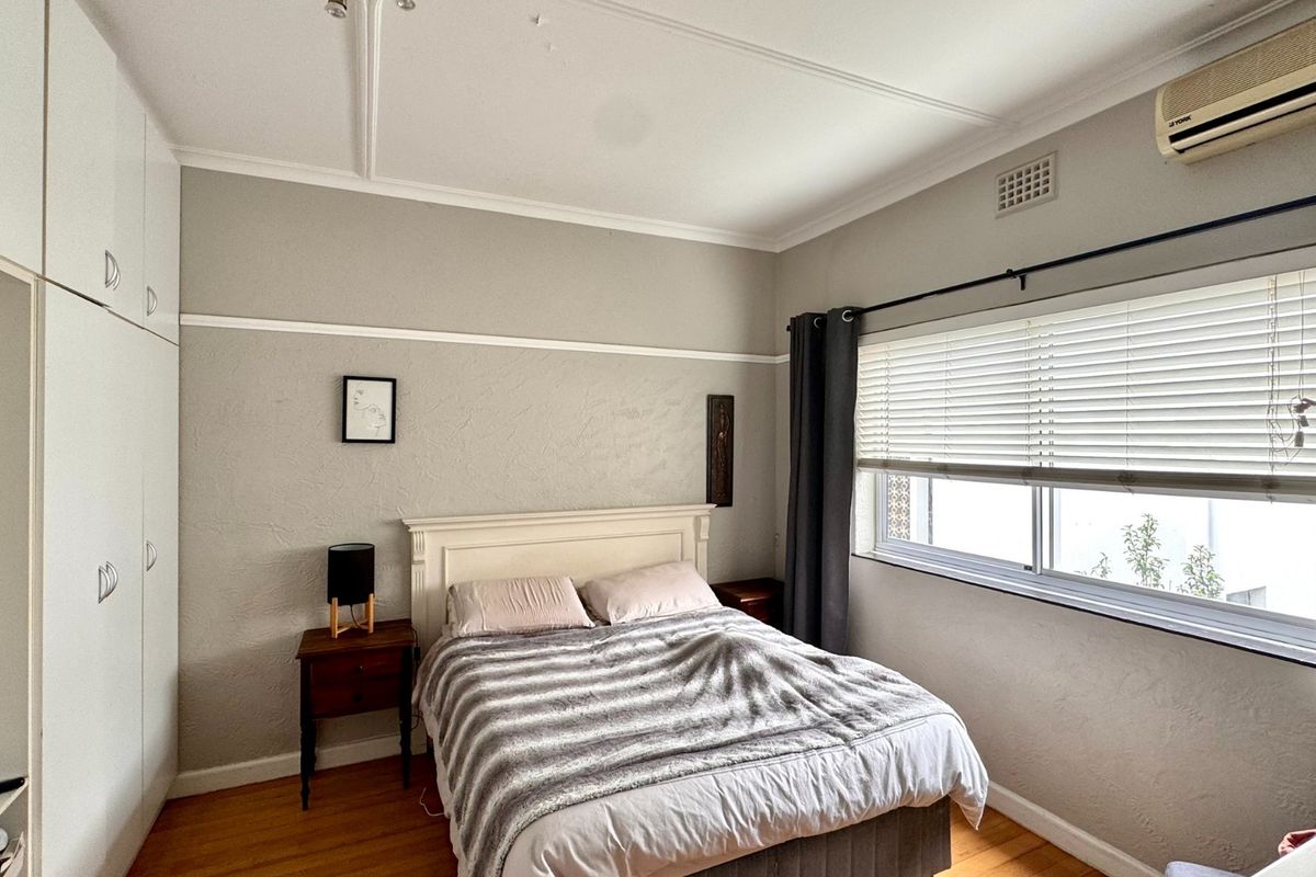 A bedroom featuring timber flooring, built-in cupboards, and a wall-mounted air conditioning unit, offering a functional space with classic architectural details.