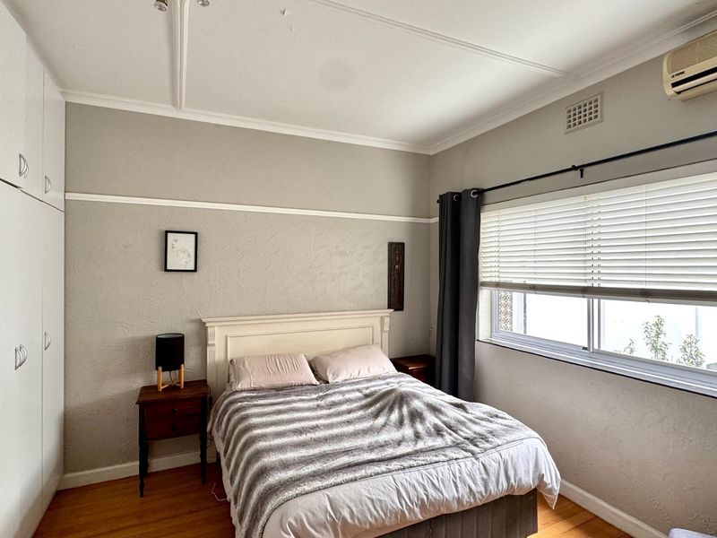 A bedroom featuring timber flooring, built-in cupboards, and a wall-mounted air conditioning unit, offering a functional space with classic architectural details.