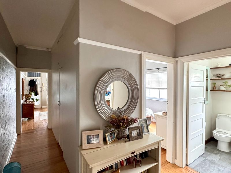 A well-maintained hallway featuring classic crown molding, warm wooden flooring, and direct access to a bathroom and adjacent living spaces.