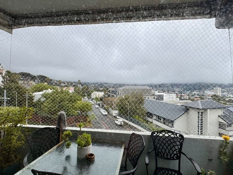 A covered balcony featuring safety netting and an elevated urban view overlooking the surrounding neighbourhood.