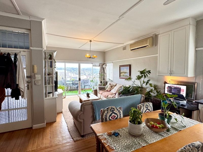Open-plan living and dining area featuring hardwood floors, built-in cabinetry, and sliding glass doors leading to a balcony with city views.