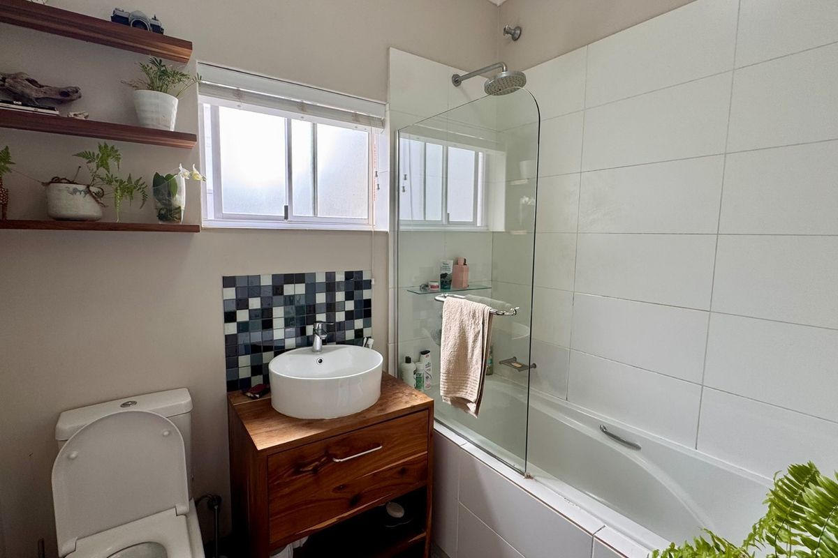 Modern bathroom featuring a wooden vanity with a vessel sink, a built-in bathtub with a glass screen, and floating wall shelves.