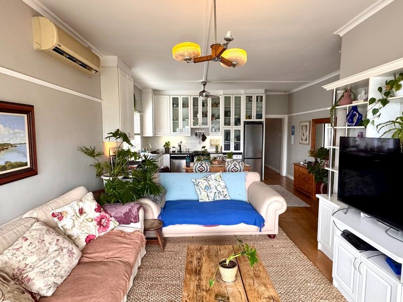 Open-plan living and kitchen area featuring hardwood floors, crown molding, built-in cabinetry, and a wall-mounted air conditioning unit.