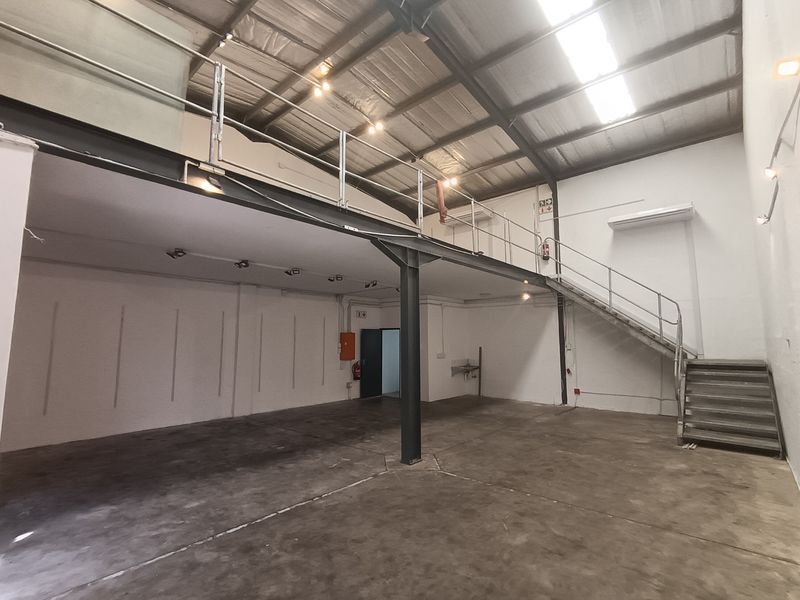 Spacious industrial unit featuring a mezzanine level, steel staircase, concrete flooring, and exposed roof trusses, suitable for various commercial or storage applications.