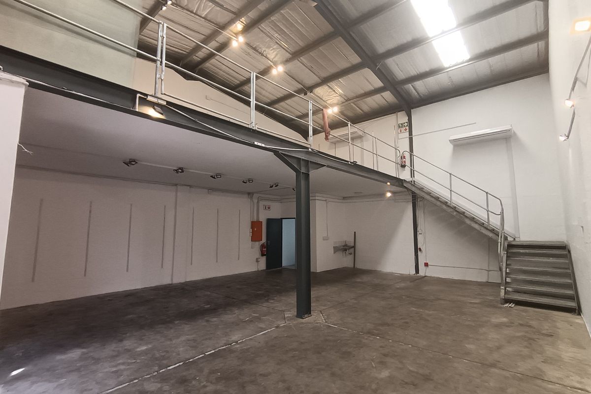 Spacious industrial unit featuring a mezzanine level, steel staircase, concrete flooring, and exposed roof trusses, suitable for various commercial or storage applications.