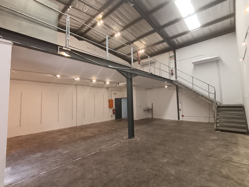 Spacious industrial warehouse unit featuring a mezzanine level, steel staircase, concrete flooring, and high ceilings with integrated skylights and industrial lighting.