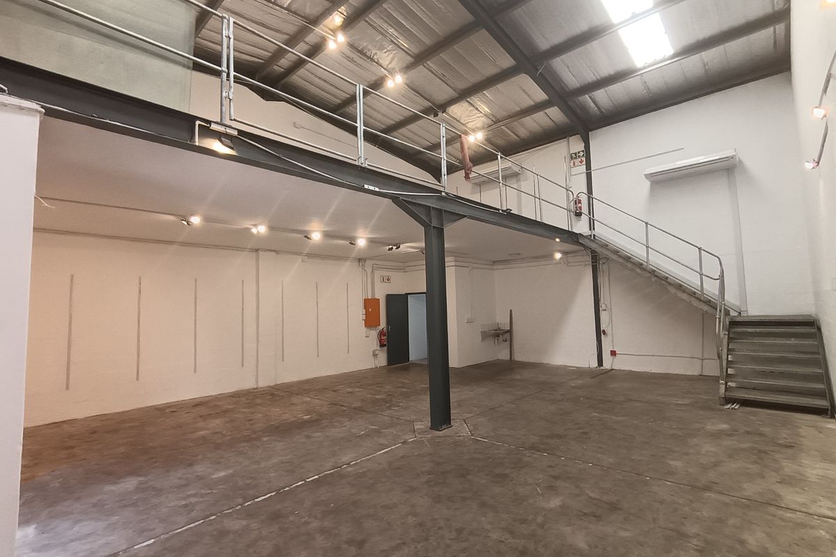 Spacious industrial warehouse unit featuring a mezzanine level, steel staircase, concrete flooring, and high ceilings with integrated skylights and industrial lighting.