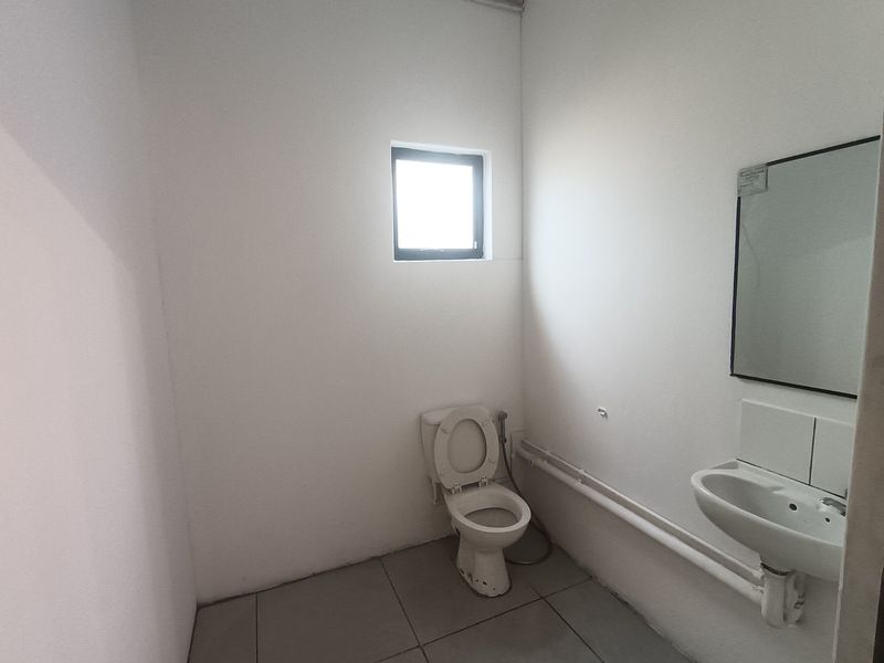 A functional, minimalist bathroom featuring a wall-mounted basin, toilet, and tiled flooring, providing a clean and practical space.