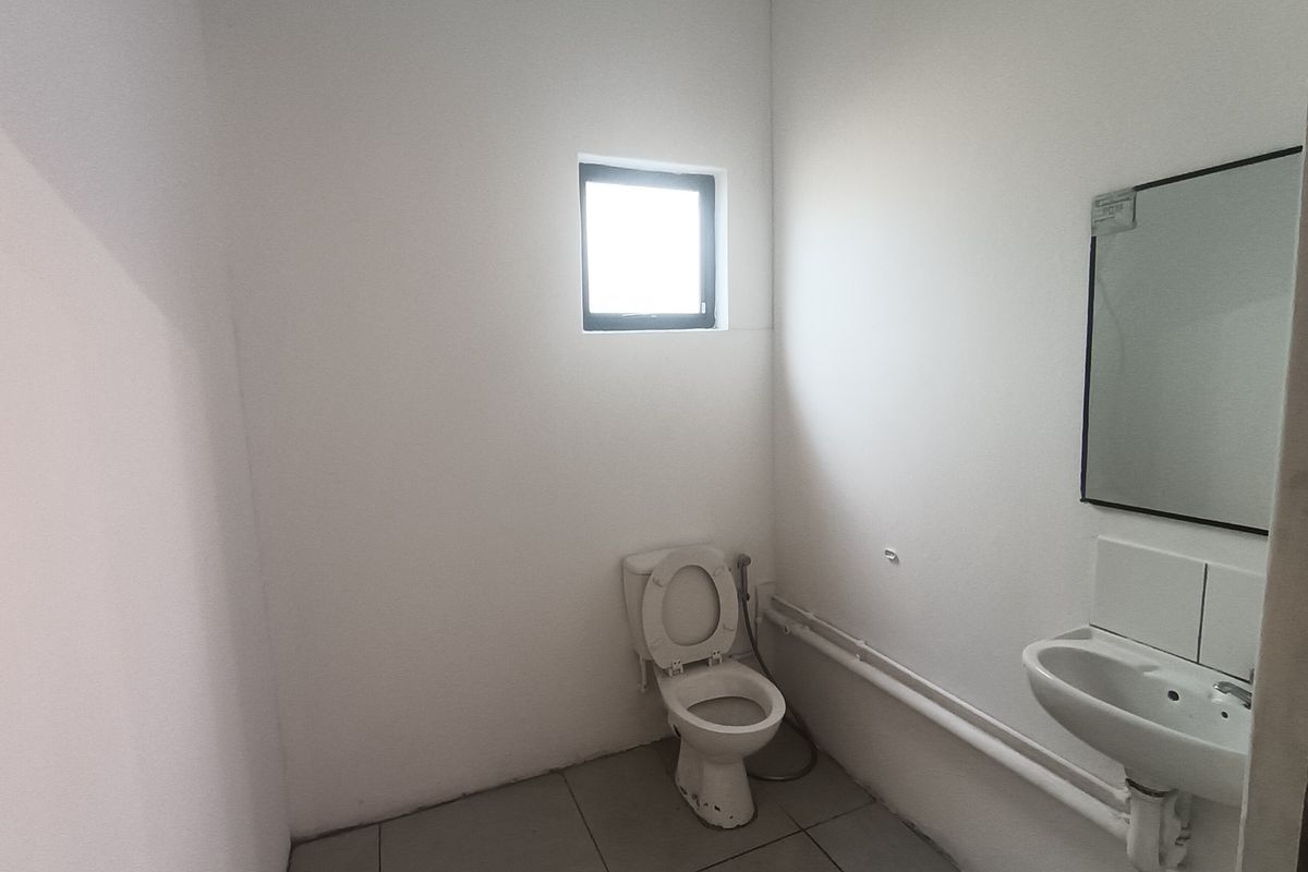 A functional, minimalist bathroom featuring a wall-mounted basin, toilet, and tiled flooring, providing a clean and practical space.