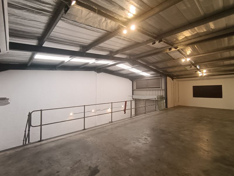 Spacious industrial mezzanine area featuring exposed steel roof structure, concrete flooring, and integrated track lighting, suitable for storage or flexible workspace.