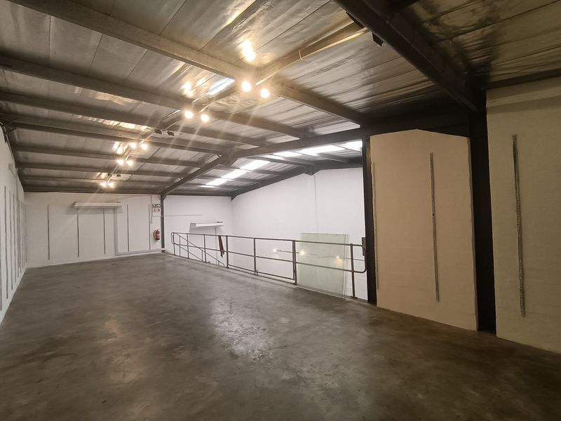 Spacious industrial mezzanine level featuring exposed steel roof trusses, concrete flooring, and a metal safety railing, suitable for storage or office conversion.