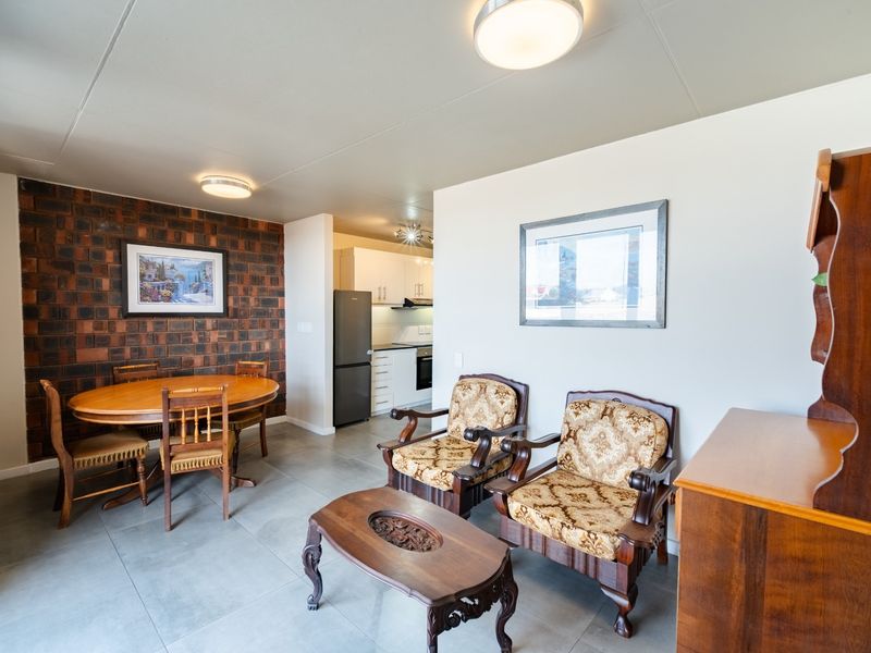 Open-plan living and dining area featuring an exposed brick wall, tiled flooring, and a functional kitchen with built-in cabinetry and appliances.