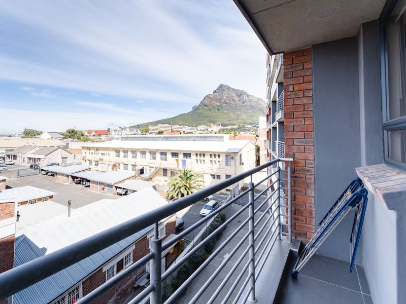 A private balcony featuring tiled flooring, metal railings, and exposed brick accents, offering expansive views of the surrounding urban landscape and mountain.