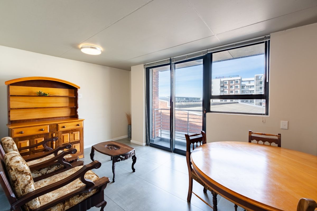 A bright living area featuring tiled flooring, a ceiling light fixture, and large sliding glass doors providing access to a balcony.