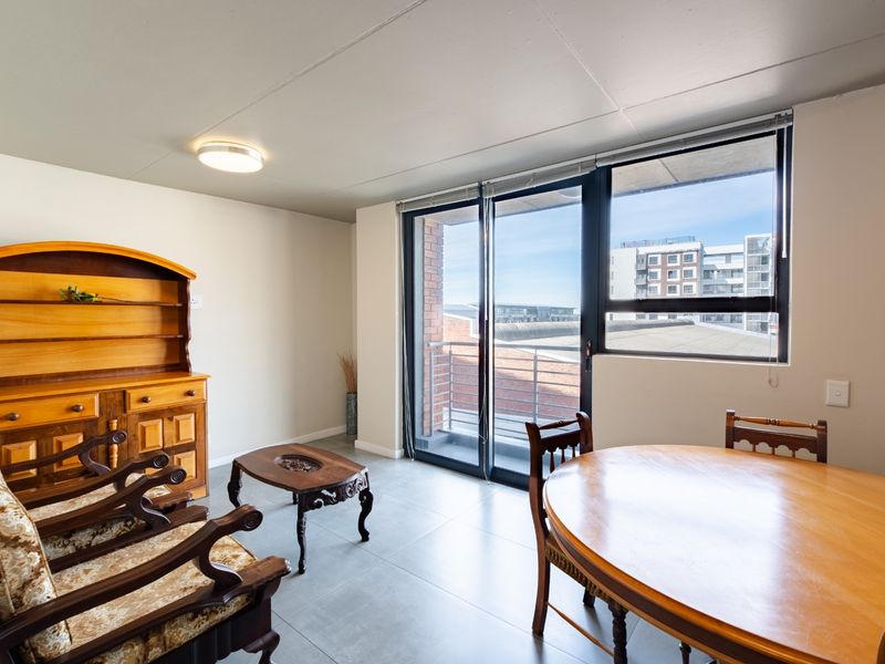 A bright living area featuring tiled flooring, a ceiling light fixture, and large sliding glass doors providing access to a balcony.