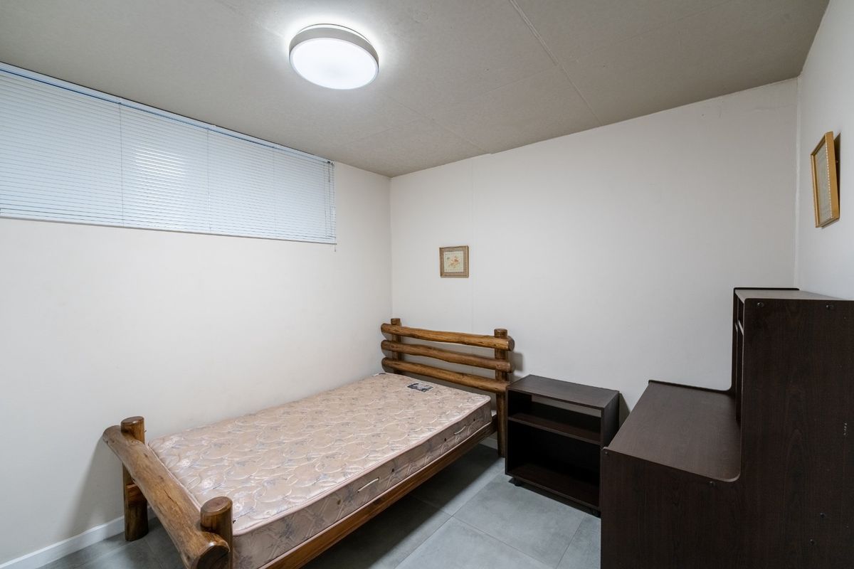 A simple bedroom featuring tiled flooring, a flush mount ceiling light, and venetian blinds, offering a functional and neutral living space.