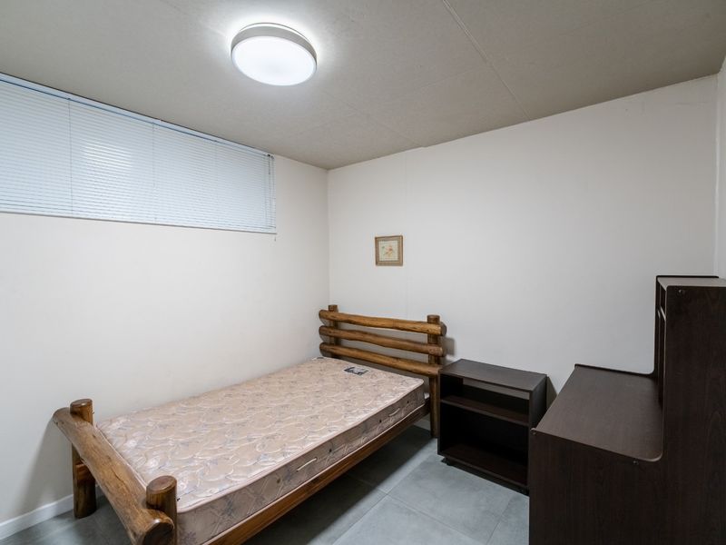 A simple bedroom featuring tiled flooring, a flush mount ceiling light, and venetian blinds, offering a functional and neutral living space.