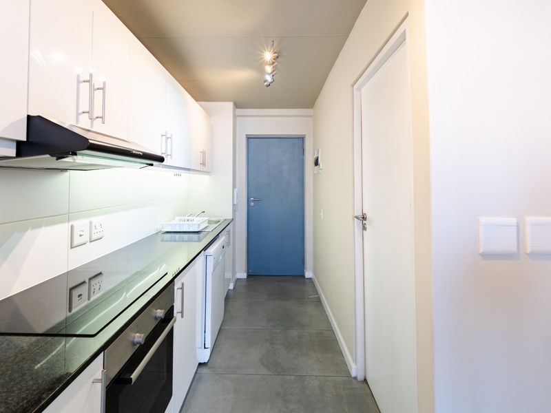 Modern galley-style kitchen featuring sleek white cabinetry, dark stone countertops, integrated oven and hob, and contemporary tiled flooring.