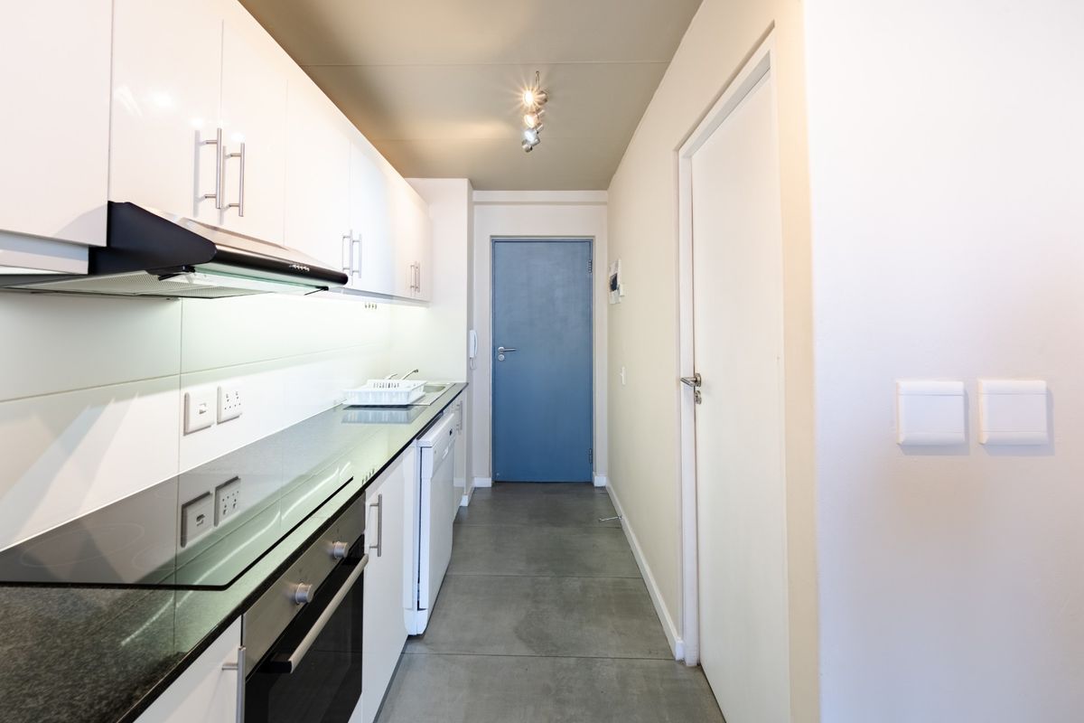 Modern galley-style kitchen featuring sleek white cabinetry, dark stone countertops, integrated oven and hob, and contemporary tiled flooring.