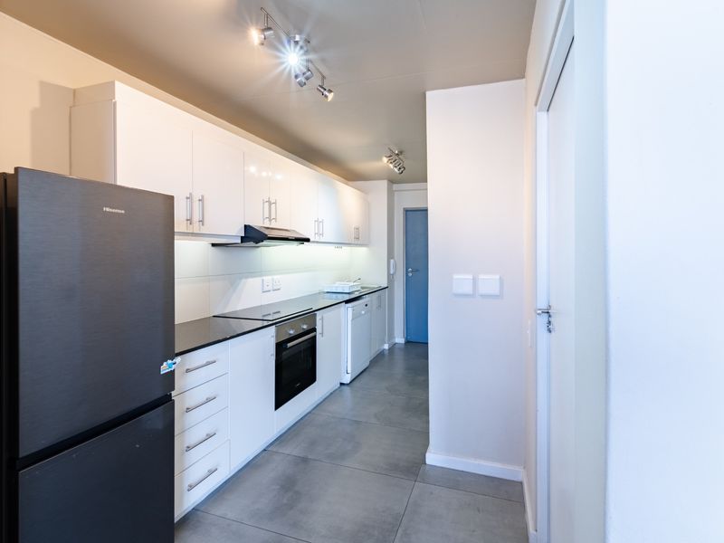 A modern, well-maintained kitchen featuring white cabinetry, black granite countertops, integrated appliances, and sleek tiled flooring.
