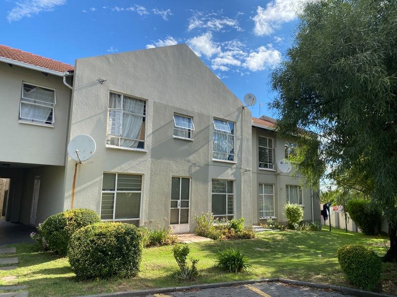 Rear elevation of a multi-story apartment building featuring a plastered facade, tiled roof, and established garden area with paved access.