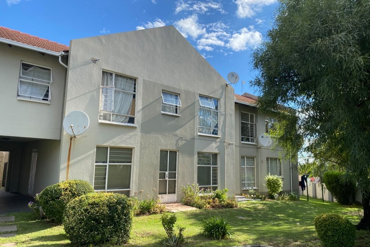 Rear elevation of a multi-story apartment building featuring a plastered facade, tiled roof, and established garden area with paved access.