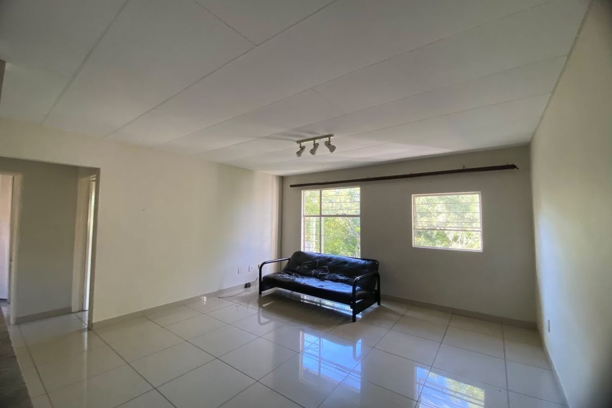 Spacious living area featuring neutral tiled flooring, ceiling track lighting, and large windows with aluminium frames, offering a blank canvas for interior design.