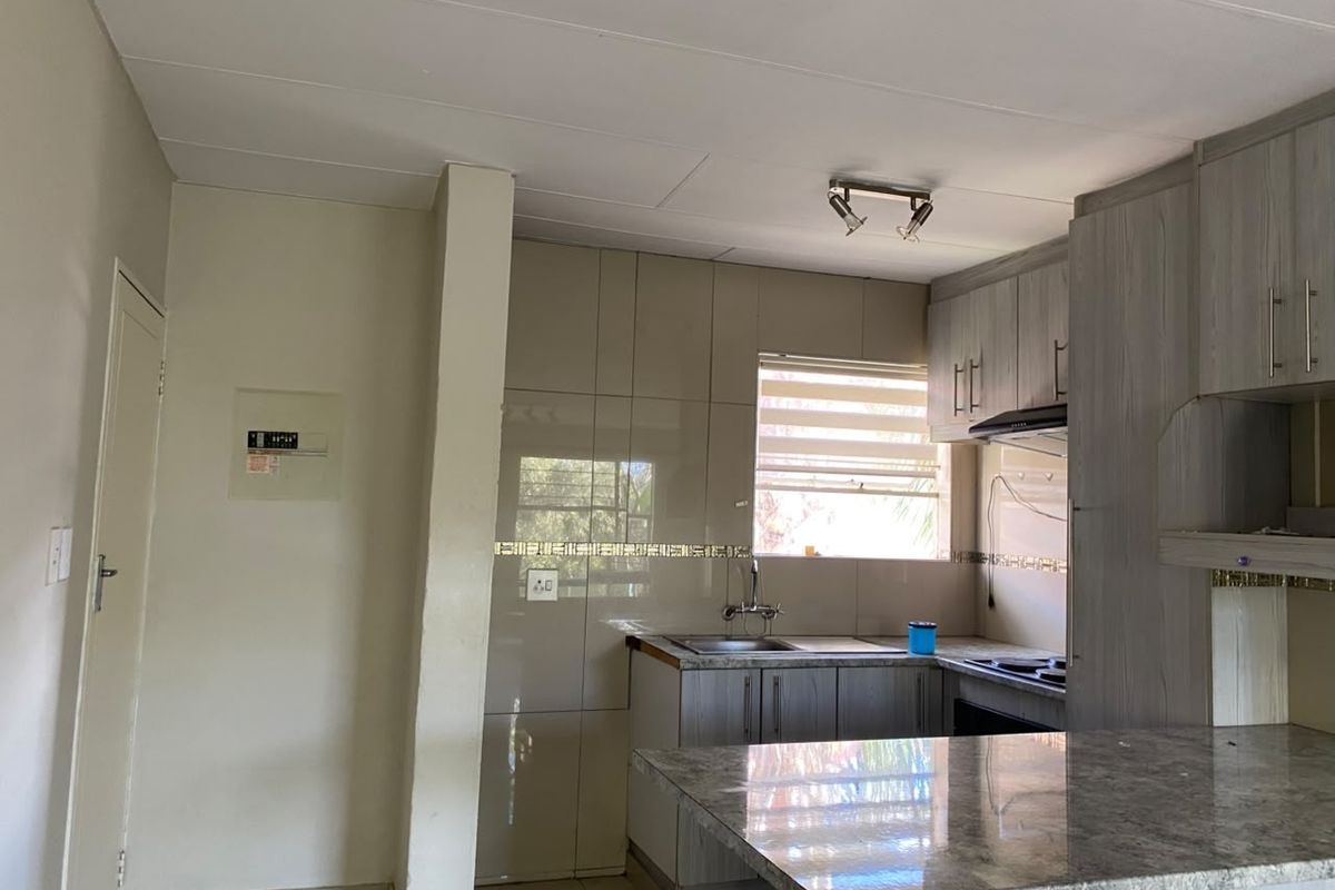 A functional kitchen featuring built-in cabinetry, a stone-look laminate countertop, tiled backsplash, and an integrated extractor fan.