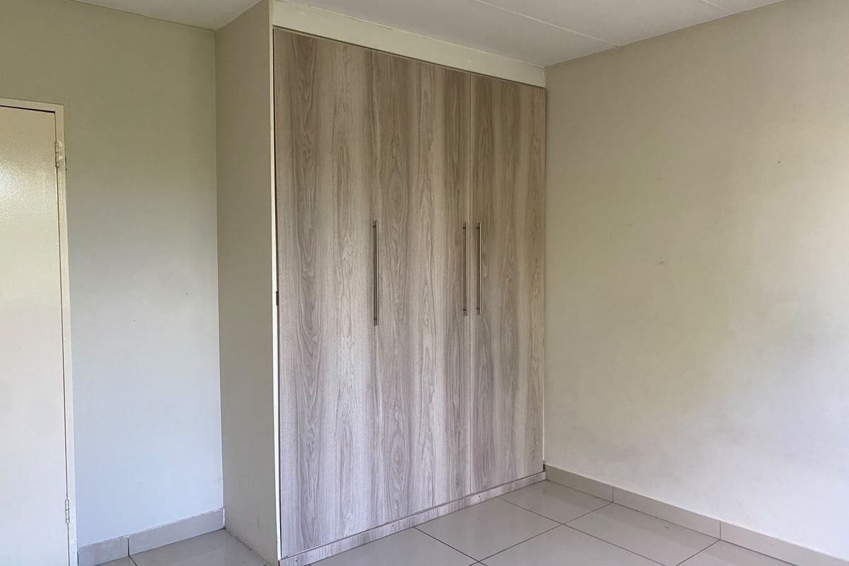 A clean, empty bedroom featuring modern wood-finish built-in wardrobes and neutral tiled flooring.