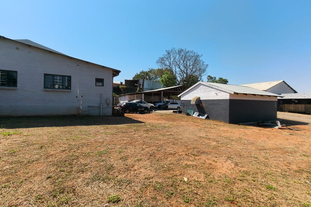 Rear exterior view of the commercial property featuring multiple outbuildings, a covered parking area, and an expansive unlandscaped yard space.