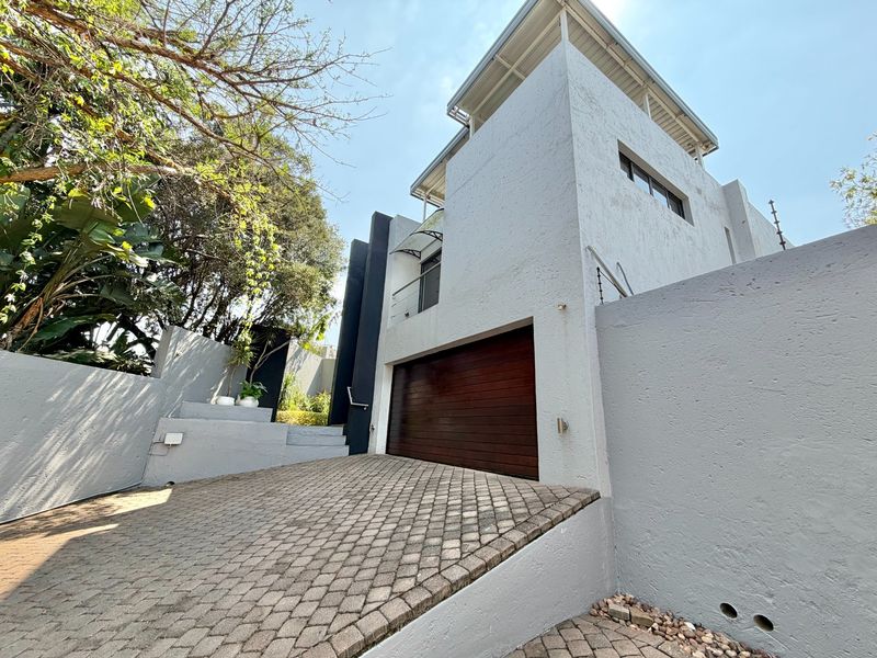 Modern multi-level residential facade featuring a paved driveway, automated garage door, and secure boundary wall with electric fencing.