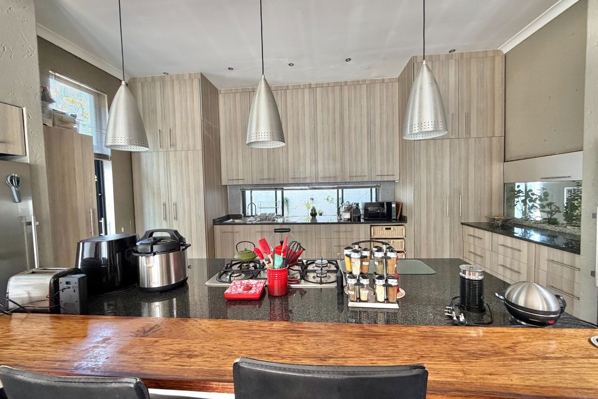 Modern kitchen featuring extensive light wood cabinetry, granite countertops, a central island with a gas hob, and stylish pendant lighting.